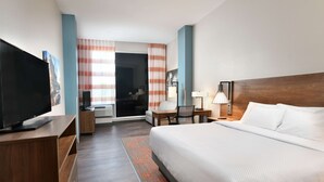 A hotel room with a large bed, a TV on a wooden stand, a desk with a chair, and a window with striped curtains. - La Quinta Inn & Ste by Wyndham Wisconsin Dells- Lake Delton (Wisconsin Dells)
