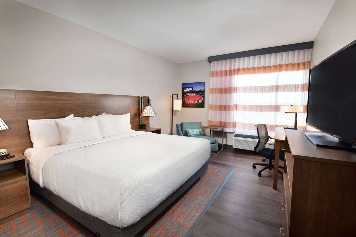 A hotel room with a large bed, a desk with a computer, a TV, and a chair.