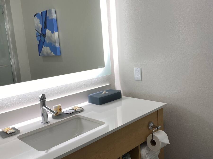 Une salle de bain moderne avec un grand miroir, un lavabo avec un robinet, un porte-serviettes et un support à papier toilette.