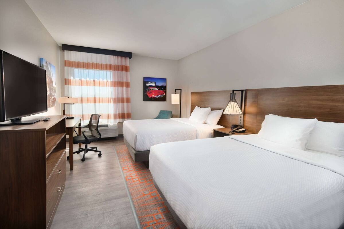 A hotel room with two beds, a desk, a TV, and a lamp.
