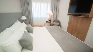 A hotel room with a large bed, a TV mounted on the wall, a desk with a lamp, and a chair.