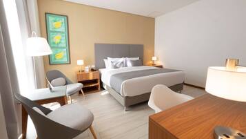 A hotel room with a bed, two bedside tables with lamps, a desk with a chair, and a wall art piece.