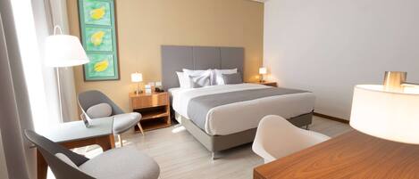 A hotel room with a bed, two bedside tables with lamps, a desk with a chair, and a wall art piece.