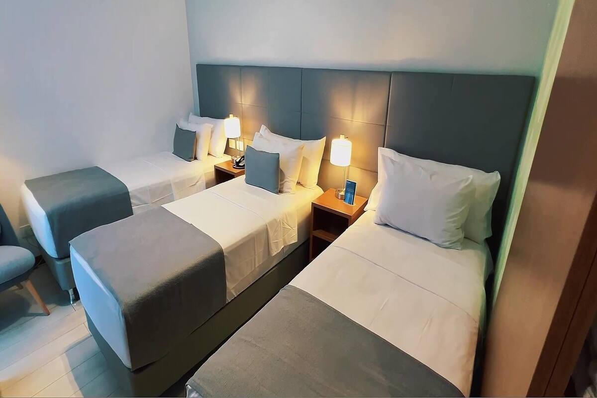 Ein Hotelzimmer mit zwei Einzelbetten, jeweils mit Nachttisch, Lampe und Kissen.