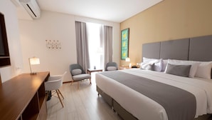 Hotellihuone, jossa on suuri sänky, työpöytä, tuoli ja lamppu.