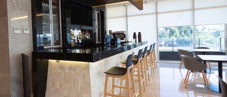 Un espace bar moderne avec un comptoir noir, des tabourets de bar en bois et une grande fenêtre offrant une vue sur l’extérieur.