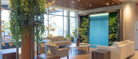 A modern lobby with a wooden ceiling, white sofas, a coffee table, and a vertical garden wall.