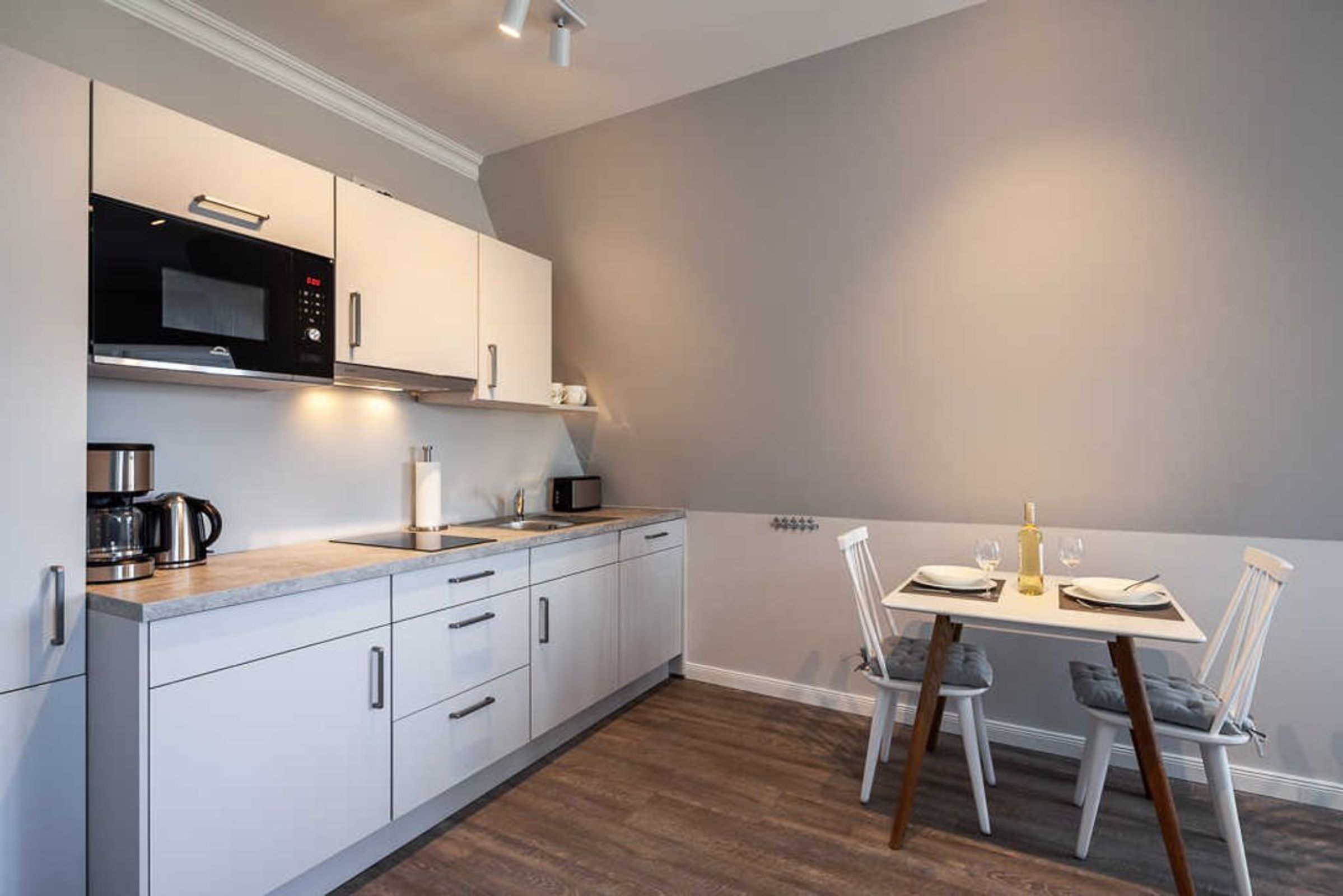 A modern kitchen with white cabinets, a built-in microwave, and a dining area with a table set for two.