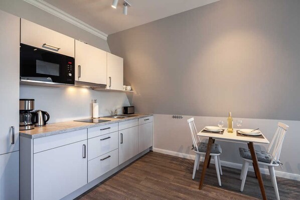 Una cocina moderna con armarios blancos, microondas integrado y una zona de comedor con una mesa dispuesta para dos personas.