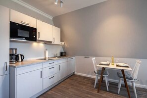 A modern kitchen with white cabinets, a built-in microwave, and a dining area with a table set for two. - App. Cardinal - cardinal (Kühlungsborn)