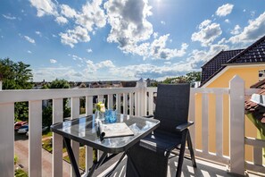 A balcony with a glass table, a chair, and a view of the neighborhood. - App. Cardinal - cardinal (Kühlungsborn)