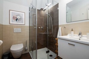 A modern bathroom with a glass-enclosed shower, a toilet, and a sink with a mirror above.
