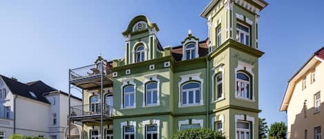 A green building with a tower, multiple windows, and a balcony.