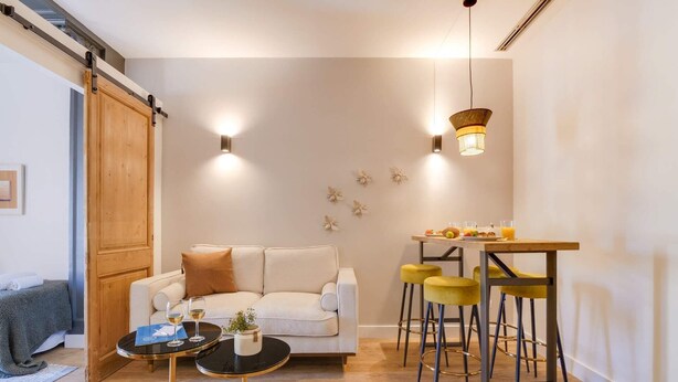 Un salon moderne avec un canapé, une table basse ronde et un coin repas équipé de tabourets.