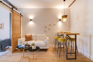 Un salon moderne avec un canapé, une table basse ronde et un coin repas équipé de tabourets.