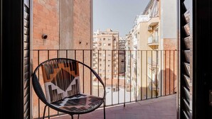 Un balcon avec un fauteuil en osier, une rambarde en métal et une vue sur un paysage urbain avec des immeubles.