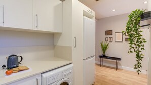 Une cuisine moderne équipée d’un lave-linge, d’une bouilloire et d’une petite table agrémentée d’une plante.