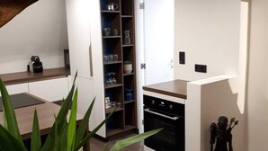 A modern kitchen with white cabinetry, a built-in oven, and a shelf unit with glassware. - Flat at Grand Place. (Brussel)