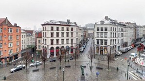 A city street with historic buildings, parked cars, and a statue in the foreground. - Flat at Grand Place. (Brussel)