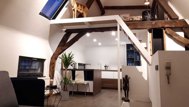 A modern loft-style living space with exposed wooden beams, a flat-screen TV, a dining area, and a staircase leading to an upper level. - Flat at Grand Place. (Brussel)