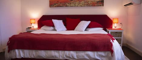 Una cama grande con cabecera roja, ropa de cama blanca y dos lámparas de noche.