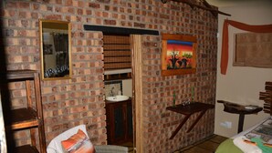 Een kamer met een bakstenen muur, een bed, een stoel, een tafeltje, een spiegel, een schilderij en een raam.