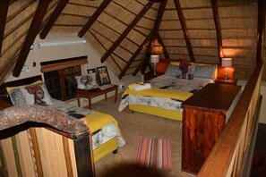 A room with two beds, a wooden bench, a small table, and a thatched roof.