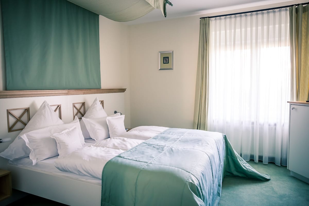 Una habitación de hotel con una cama, una mesita de noche, un cuadro en la pared y una ventana con cortinas.
