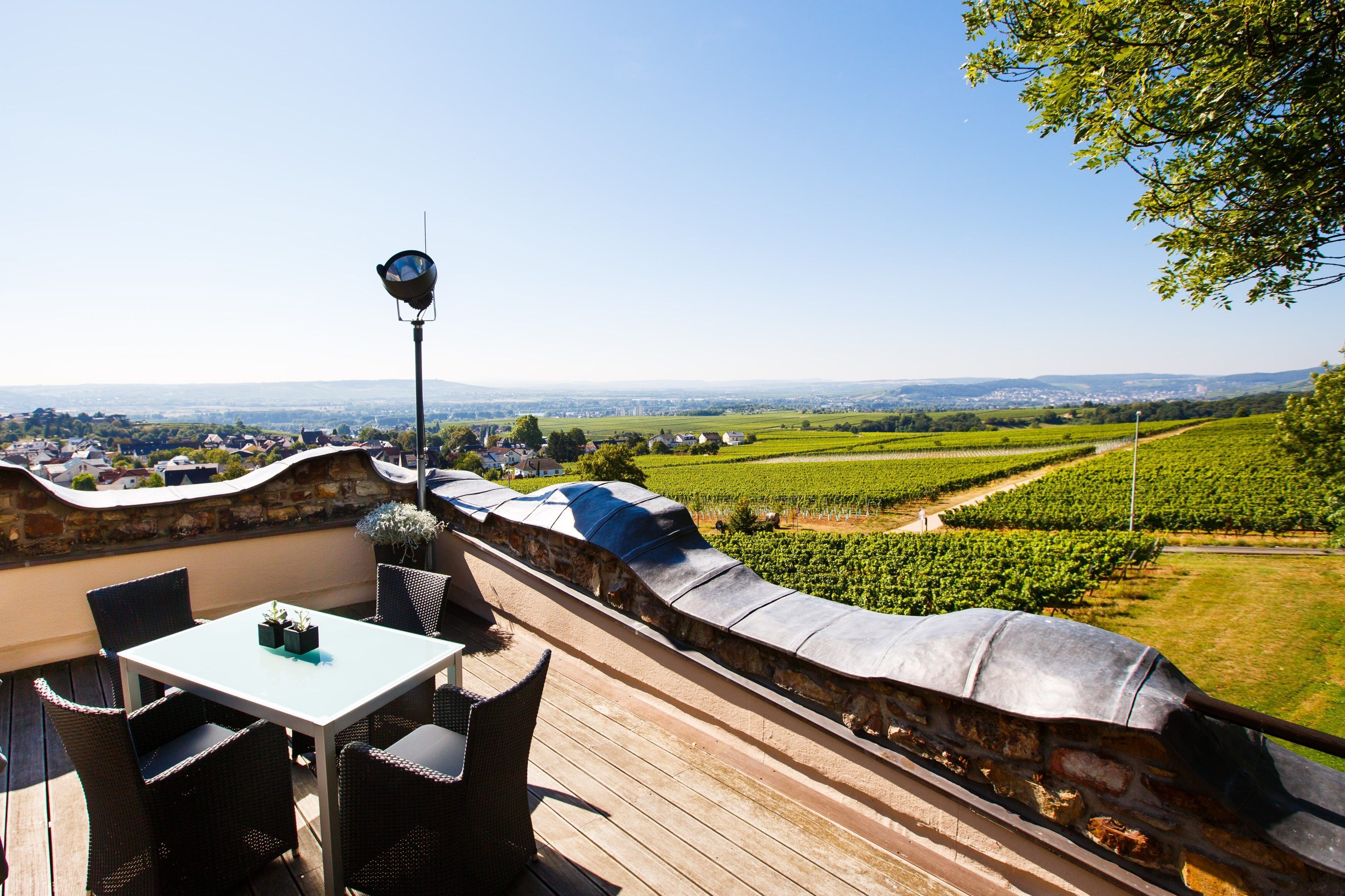 A terrace with a table and chairs, overlooking a vineyard and distant town.