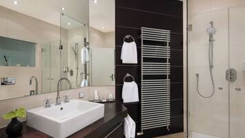 Un baño moderno con un lavamanos grande, un espejo, un perchero para toallas y una ducha con mampara de vidrio.