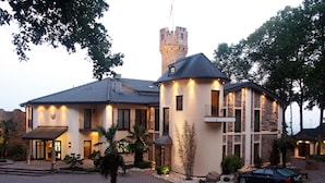Un edificio grande de estilo castillo con torre, un patio cubierto y un coche estacionado adelante.