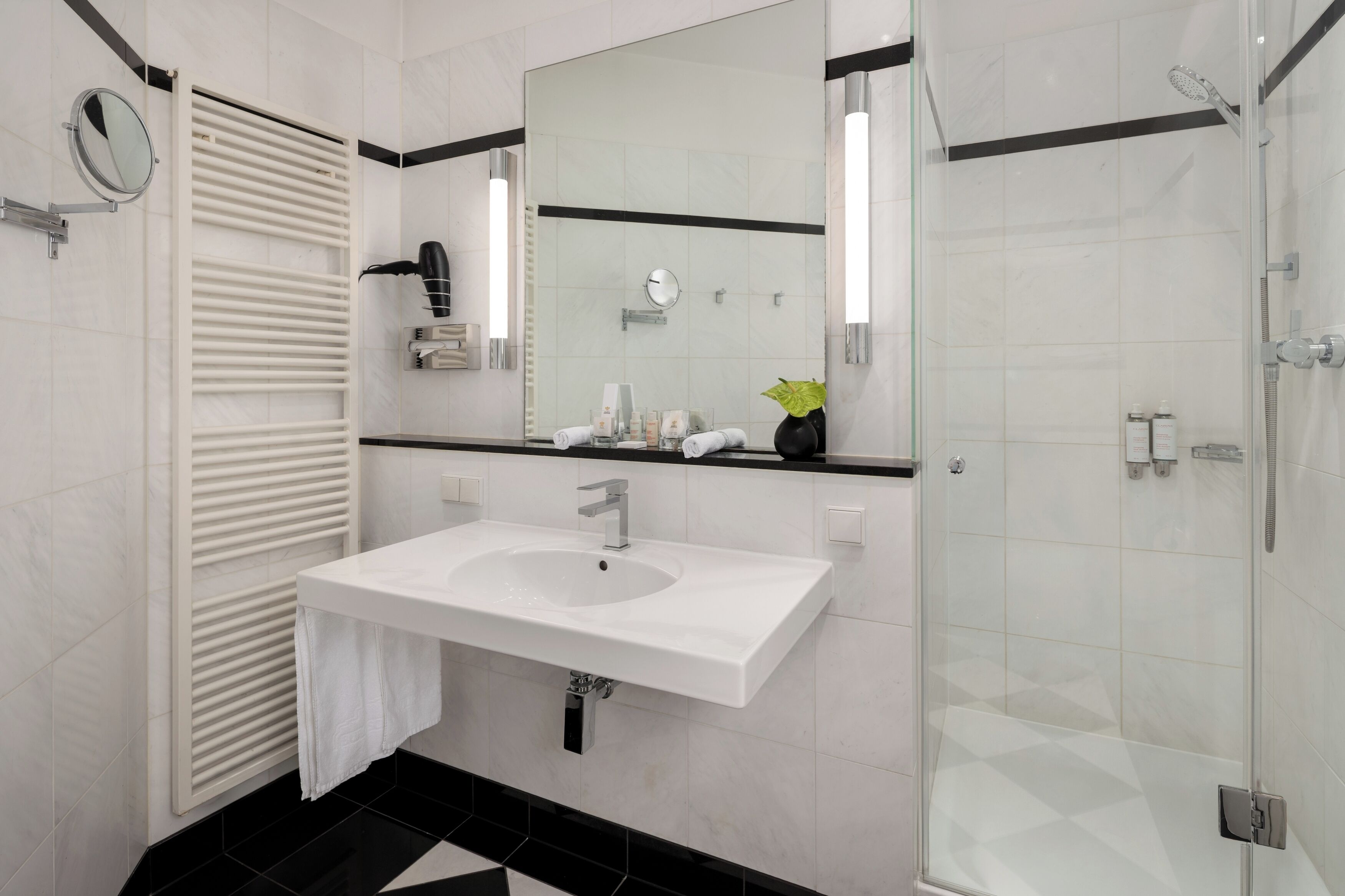 Un baño moderno con lavamanos blanco, espejo, toallero y cabina de ducha con mampara de vidrio.