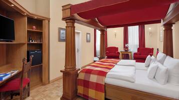 A hotel room with a bed, a TV, a desk, and a red canopy.