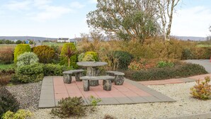 A garden with a stone table and benches, surrounded by various shrubs and trees. - Ellen's Cottage (Mountcharles)