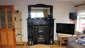 A living room with a fireplace, a television, a sofa, and a wooden table. - Ellen's Cottage (Mountcharles)