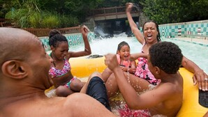 A group of people in a water park, including a man and a woman in a pink floral swimsuit, and a child in a yellow float.