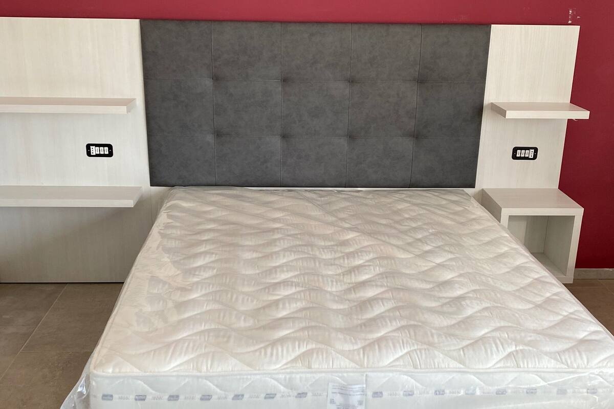 Un lit avec une tête de lit rembourrée de couleur grise, des tables de chevet blanches et un mur rouge.