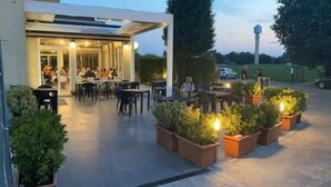 An outdoor patio area with tables and chairs, surrounded by potted plants and a covered seating area. - B&B Bertani (Modena)