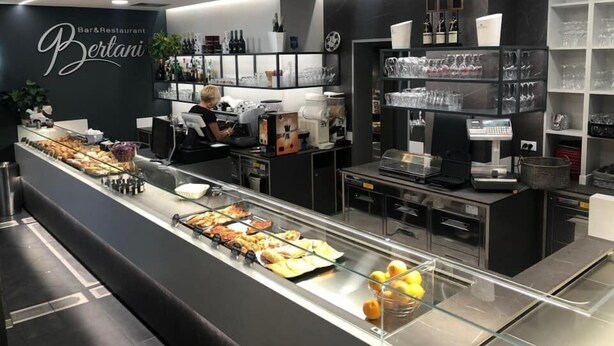 A modern bar and restaurant interior with a long counter displaying various food items and a coffee machine. - B&B Bertani (Modena)