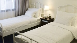 Hotellihuone, jossa on kaksi erillistä sänkyä, kattokruunu, ilmastointilaite ja ikkuna, jossa on verhot.