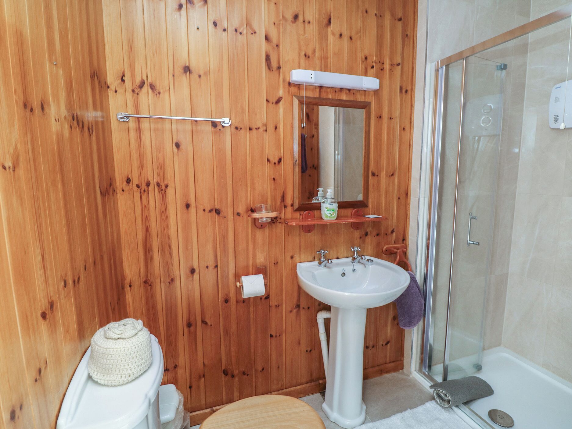 Un baño con paneles de madera, un lavabo, un espejo, un perchero para toallas y una ducha.