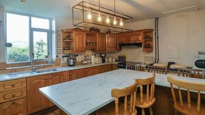A kitchen with wooden cabinets, a marble countertop, and a dining area with wooden chairs. - Cairbre House (Dungarvan)