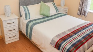 Un dormitorio ordenado con cama, dos mesitas de noche y una ventana con cortinas.
