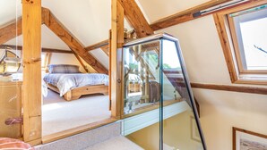 A bedroom with a glass-enclosed bed, wooden beams, and a window. - Swallows Loft (Kingsbridge)