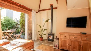 A cozy living room with a leather sofa, wooden cabinets, a TV, and a fireplace. - Swallows Loft (Kingsbridge)