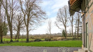 Eine Terrasse mit einem Metalltisch und -stühlen, ein Kiesweg und Blick auf ein grünes Feld und Bäume.