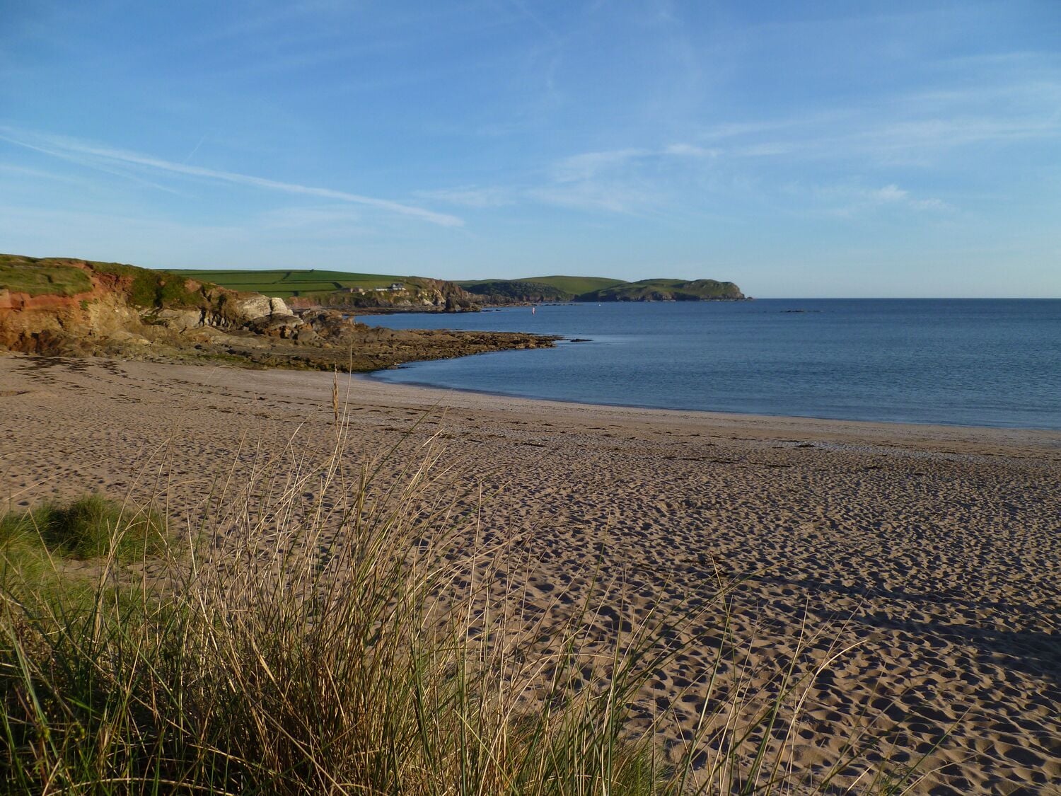 Une plage de sable avec des dunes herbeuses et une mer calme.