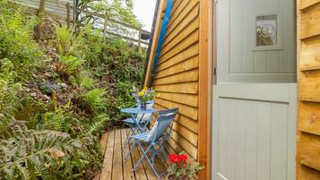 A wooden deck with a table and chairs, surrounded by lush greenery and ferns.