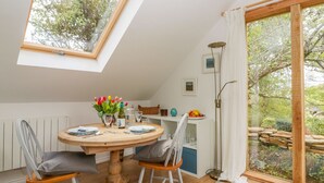Un comedor con una mesa redonda de madera, dos sillas, un jarrón de tulipanes y vistas al jardín a través de un ventanal.