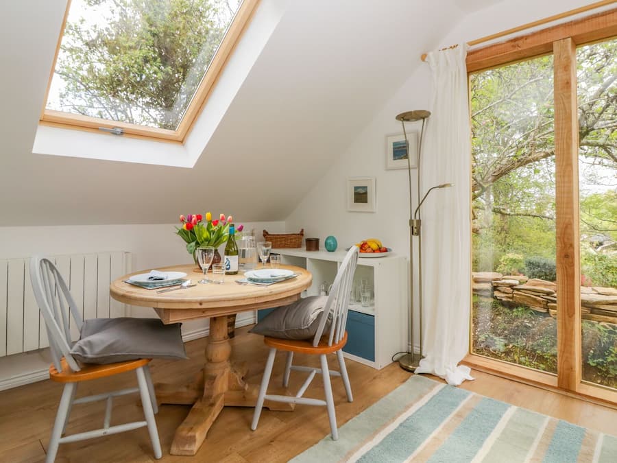 Un coin repas avec une table ronde en bois, deux chaises, un vase de tulipes et une vue sur le jardin, visible à travers une porte vitrée.